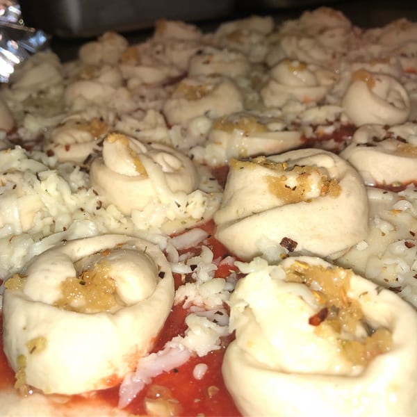 Close-up of uncooked Valentino's pizza with garlic knots, tomato sauce, and shredded cheese.