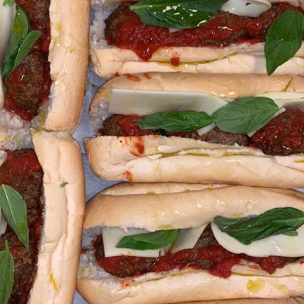 Valentino’s meatball subs with marinara, melted cheese, and fresh basil on hoagie rolls.